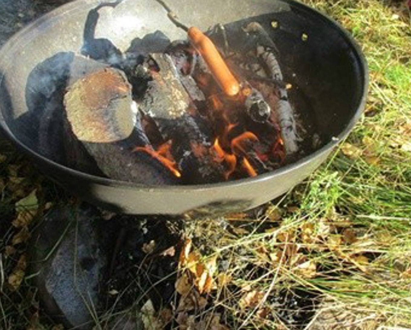 Ekte fotografi av bål med ved og matlaging i naturen ved Kringla Friluftsbarnehage. Ingen personer er synlige.